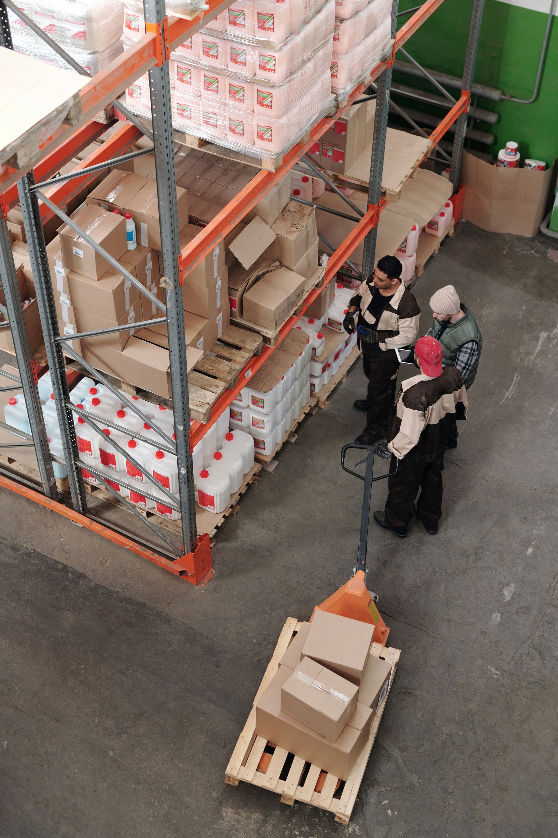 Warehouse staff reviewing cargo beside stored goods and a pallet jack